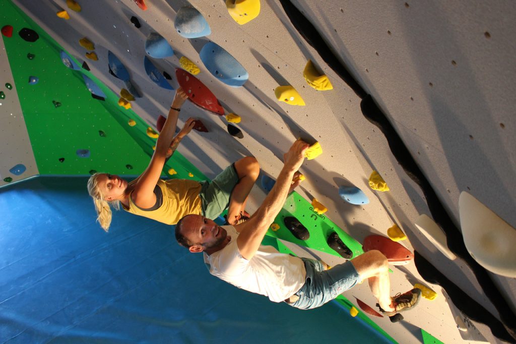 Ein Mann und eine Frau halten sich ca. 2 Meter über dem Boden an einer Kletterwand fest.