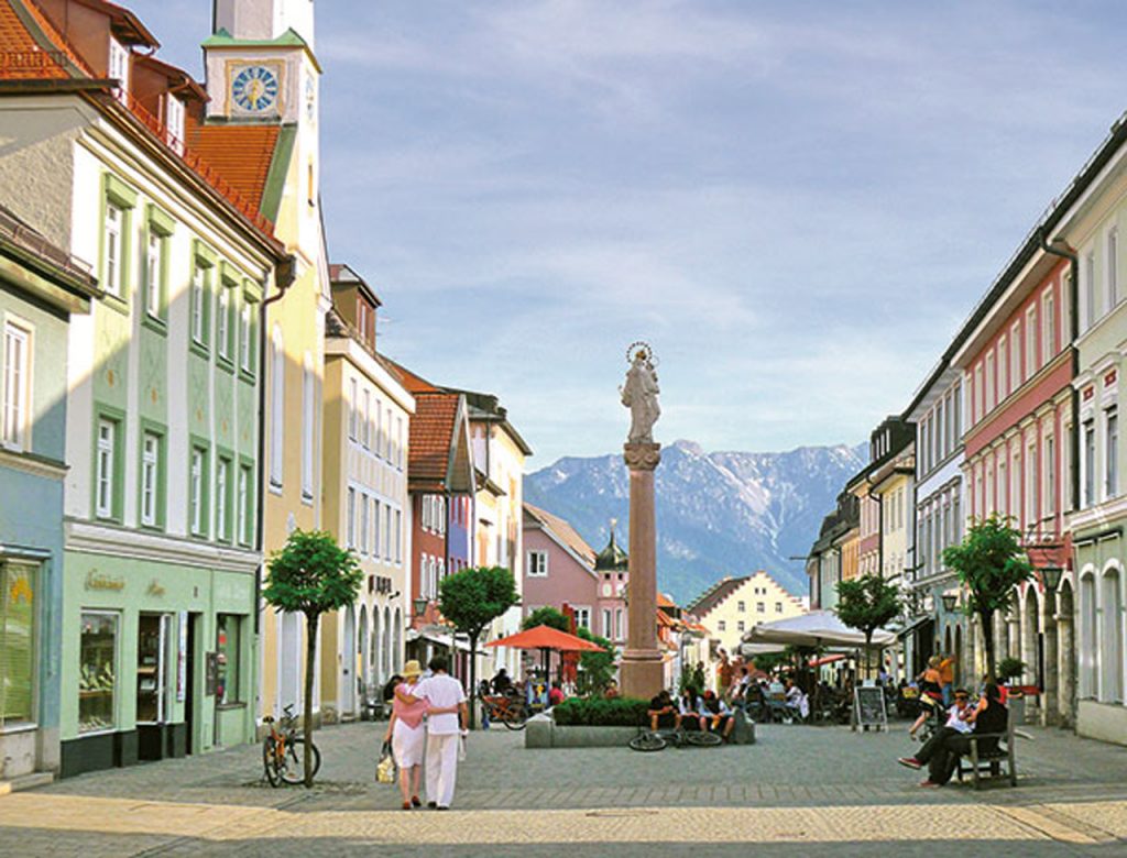 Fußgänger laufen durch eine breite Kopfsteinpflasterstraße. Links und rechts Einkaufsgeschäfte und Läden.