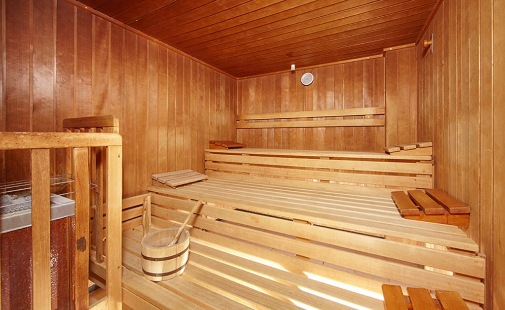 In einem kleinen Holzverkleideten Raum stehen neue Holzbänke und ein Ofen.