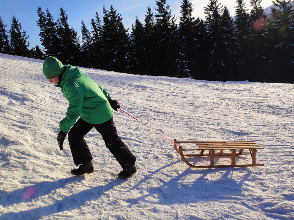 Ein Kind zieht seinen Holzschlitten im Schnee.