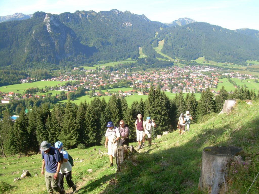 Eine Gästegruppe wandert in Zweierpärchen einen Berg hinauf Der Hintermann hält sich am Vordermann fest.